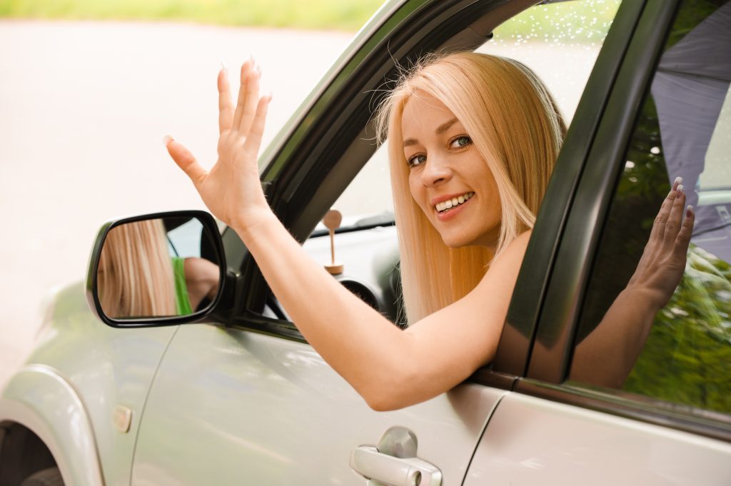 Femme au volant d'une voiture qui fait bonjour